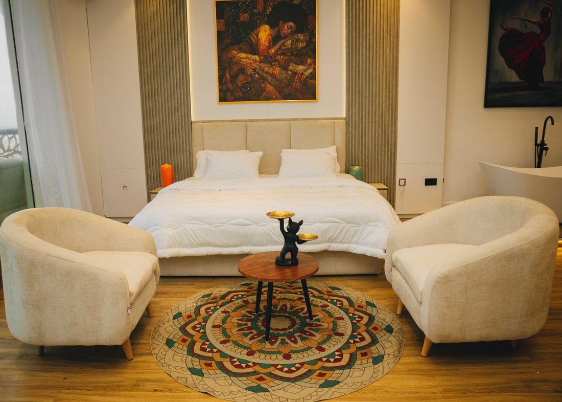 A bedroom with two armchairs, a patterned rug and a bath beyond