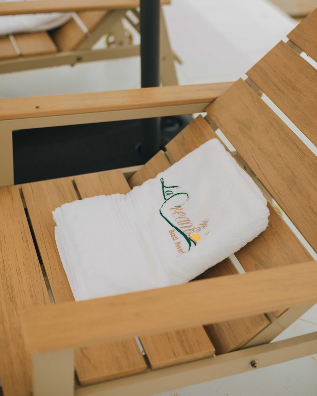 A folded white towel embroidered with the La Cream logo on a teak lounger